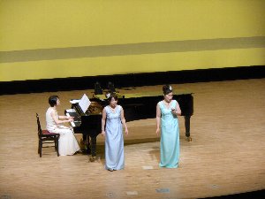 ステージの上でピアノ演奏と二人の歌手が演奏している写真