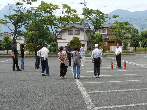 白線がひかれたアスファルト上で消火器の使い方を学ぶ人たちの写真