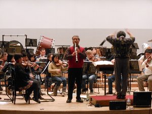指揮者と立ち上がり縦笛を吹く男性の写真