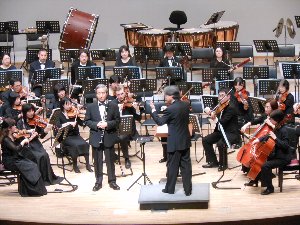 ホールで演奏する楽団とそれを指揮する指揮者の写真